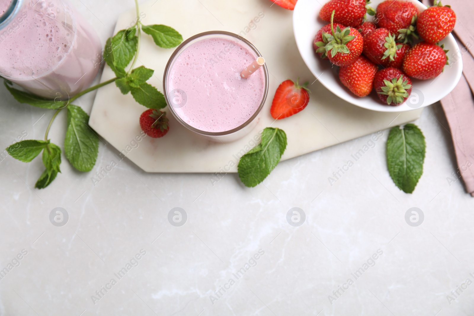 Photo of Tasty milk shake with strawberries on light grey marble table, flat lay. Space for text