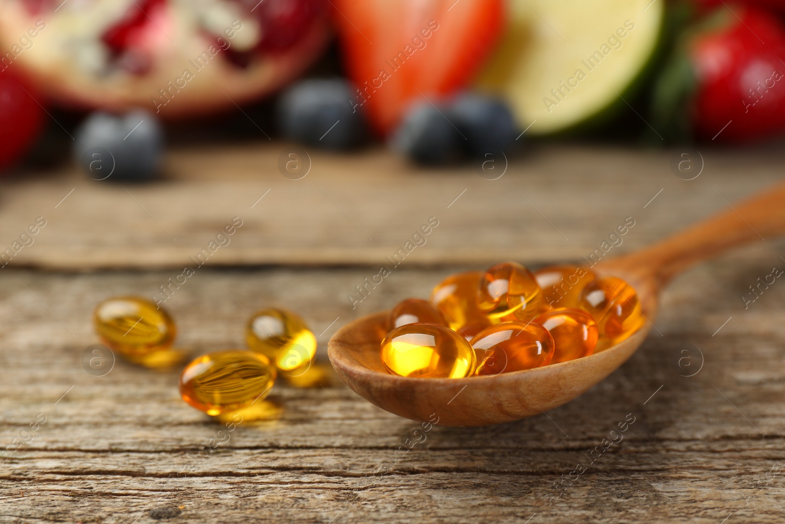 Photo of Vitamin pills in spoon on wooden table, closeup