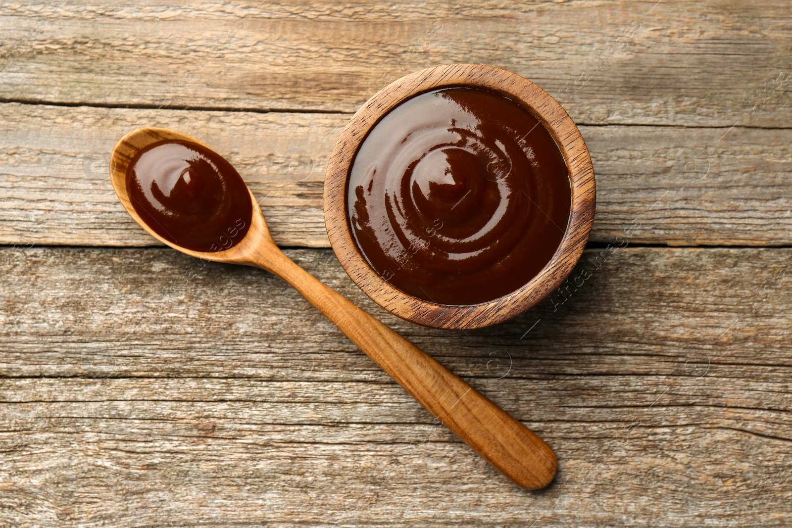 Photo of Tasty barbeque sauce in bowl and spoon on wooden table, top view