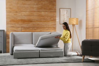 Photo of Young woman unfolding sofa into a bed in room. Modern interior