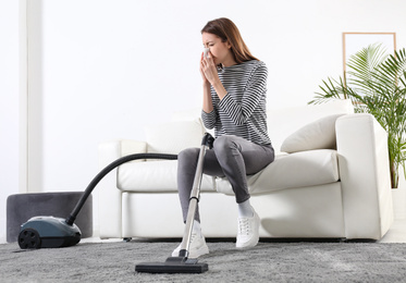 Photo of Young woman suffering from dust allergy while vacuuming house