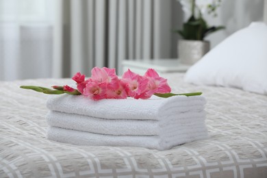 Stack of clean towels and gladiolus flowers on bed indoors