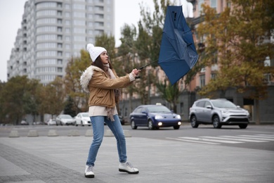 Woman with blue umbrella caught in gust of wind on street