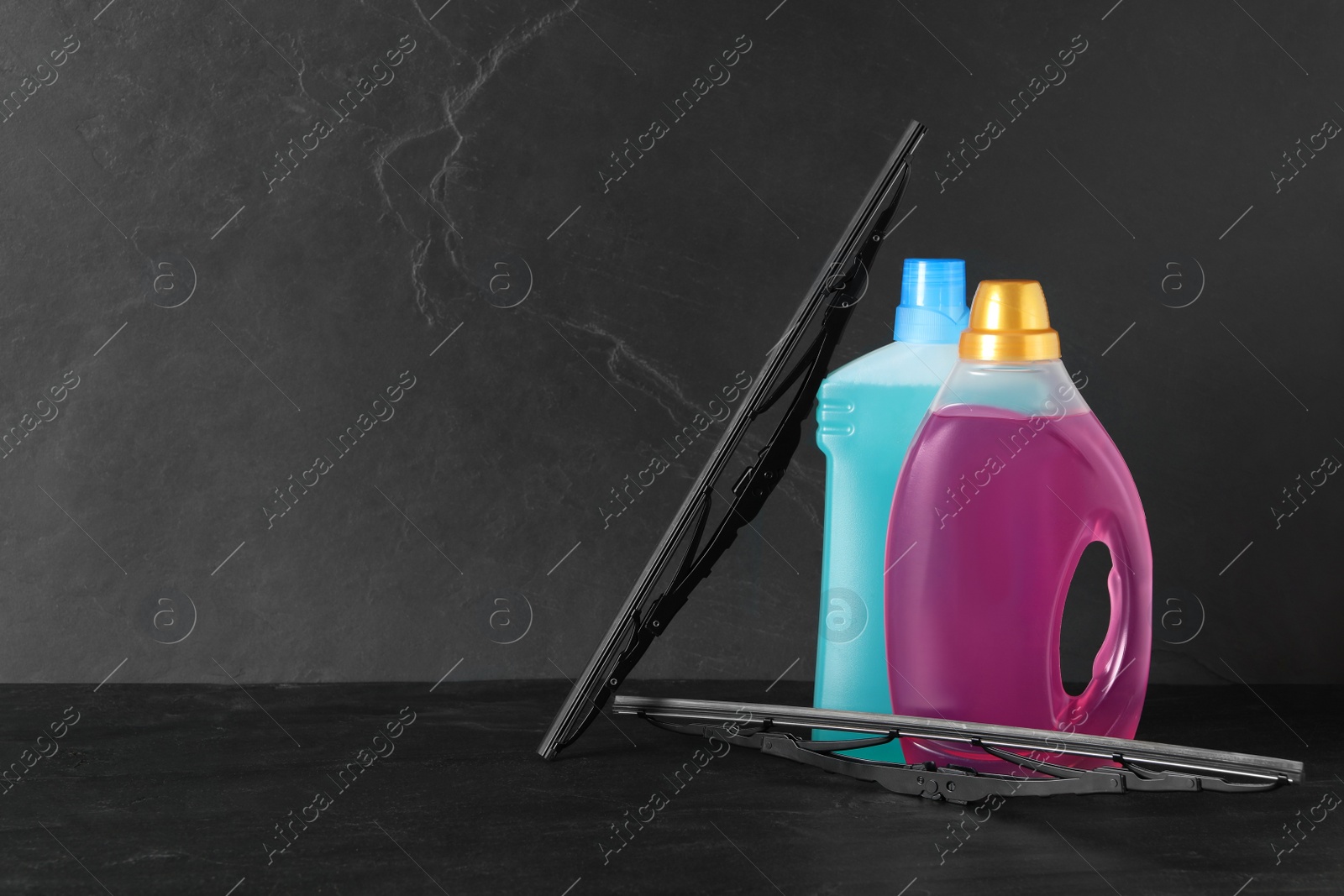 Photo of Bottles of windshield washer fluids and wipers on black table. Space for text