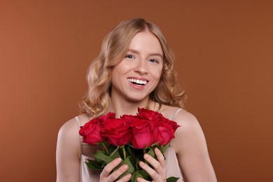 Photo of Beautiful woman with blonde hair holding bouquet of red roses on brown background
