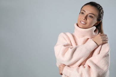 Young woman in stylish pink sweater on grey background, space for text