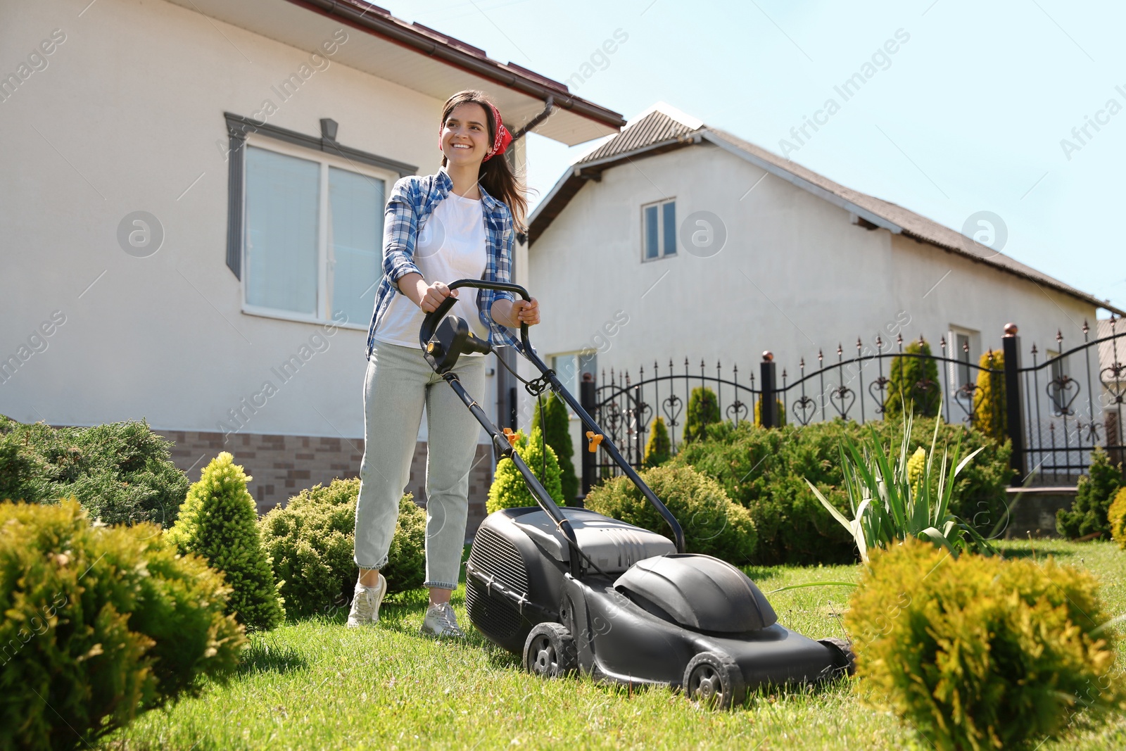 Photo of Woman cutting green grass with lawn mower in garden