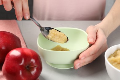 Photo of Healthy baby food. Woman putting delicious apple puree into bowl at light grey table, closeup