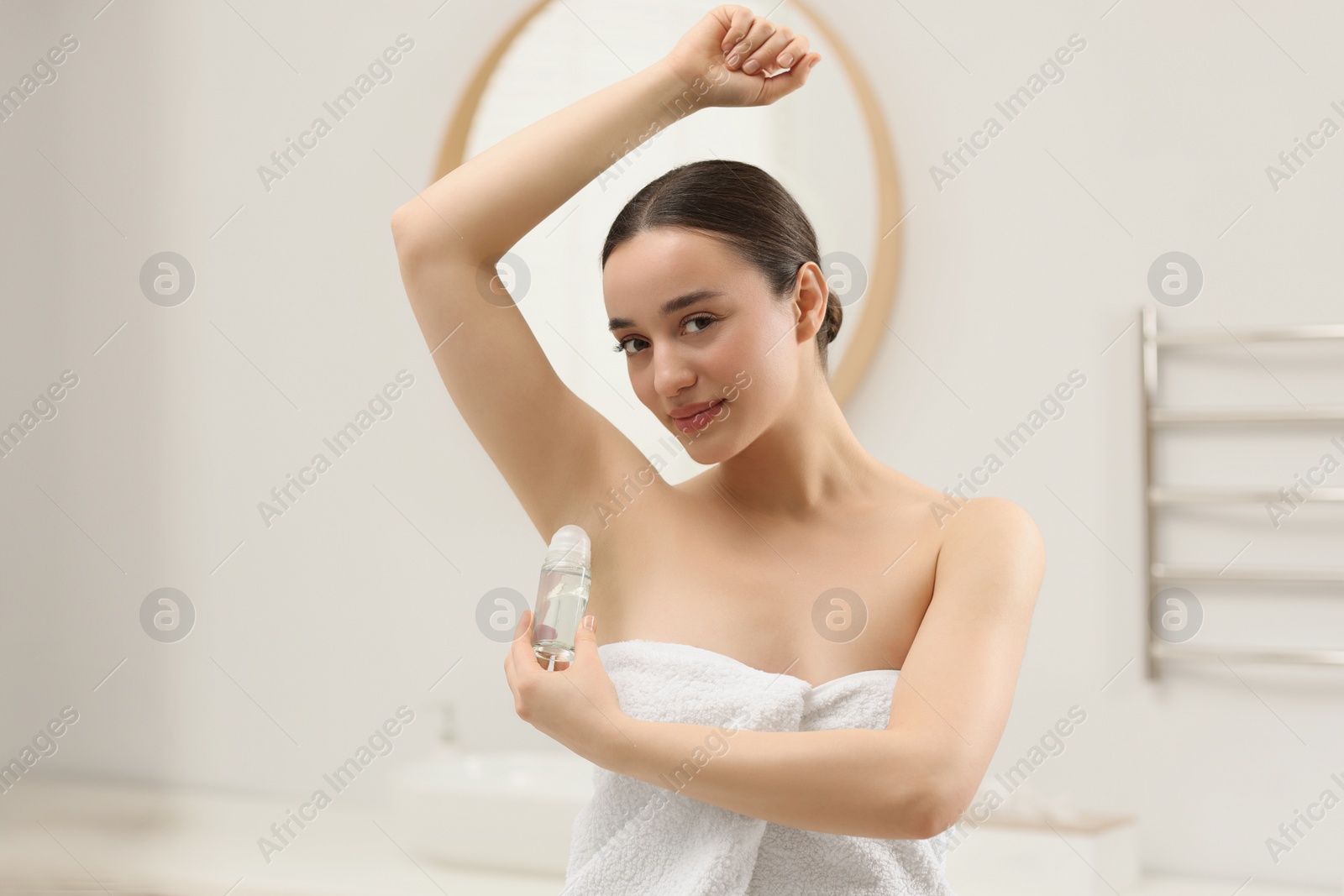 Photo of Beautiful young woman applying deodorant in bathroom