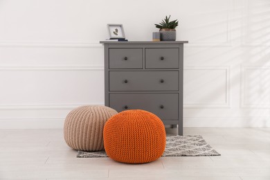 Stylish room interior with grey chest of drawers and poufs near white wall