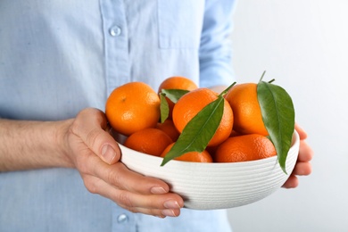 Photo of Woman holding bowl with fresh tangerines on light background, closeup