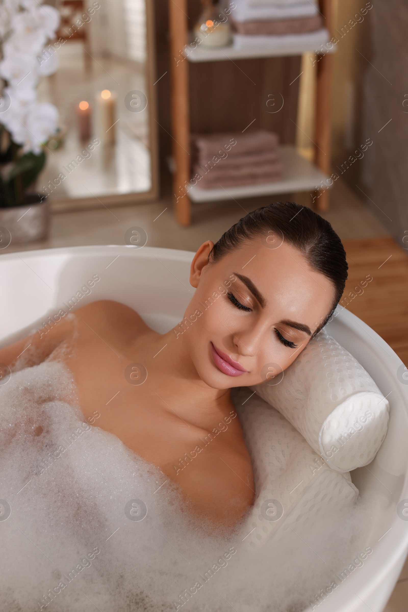 Photo of Young woman using pillow while enjoying bubble bath indoors