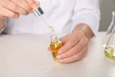 Photo of Dermatologist developing cosmetic oil at white table, closeup