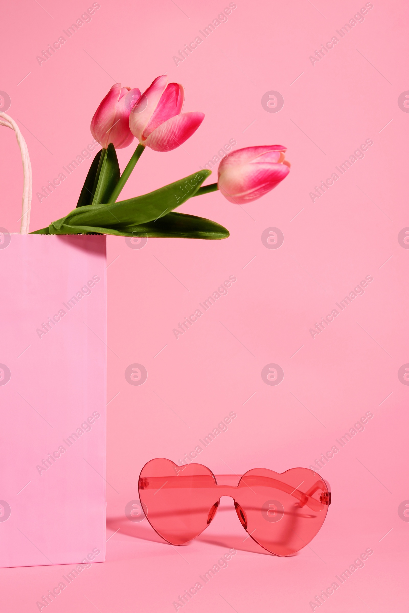 Photo of Shopping bag with beautiful tulips and stylish sunglasses on pink background