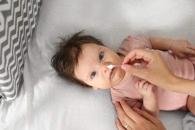 Mother cleaning nose of her baby with cotton bud on bed, closeup