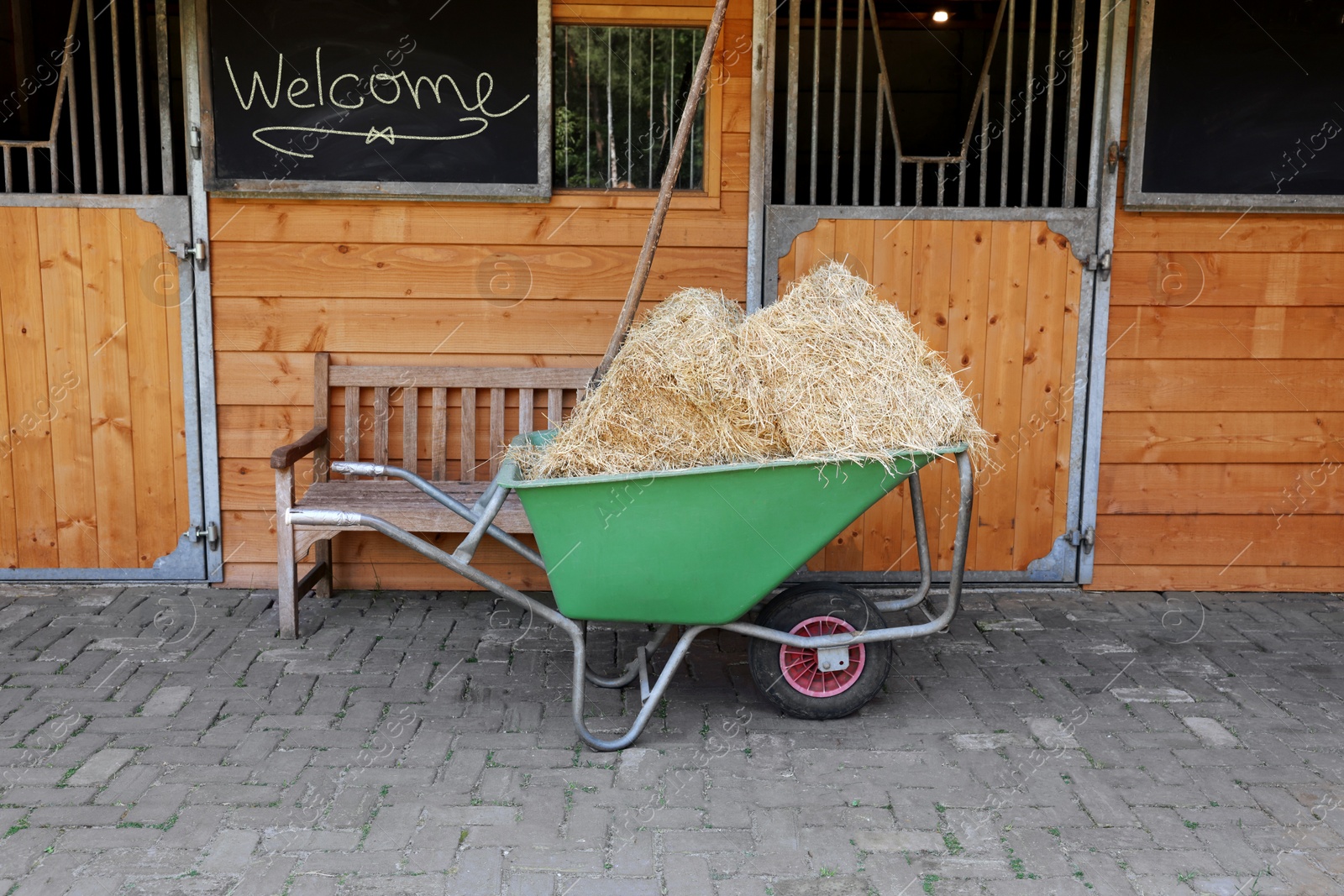 Photo of Wheelbarrow with hay near wooden stable outdoors