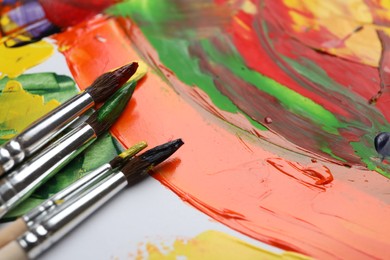 Photo of Set of brushes with different paints on artwork, closeup. Space for text