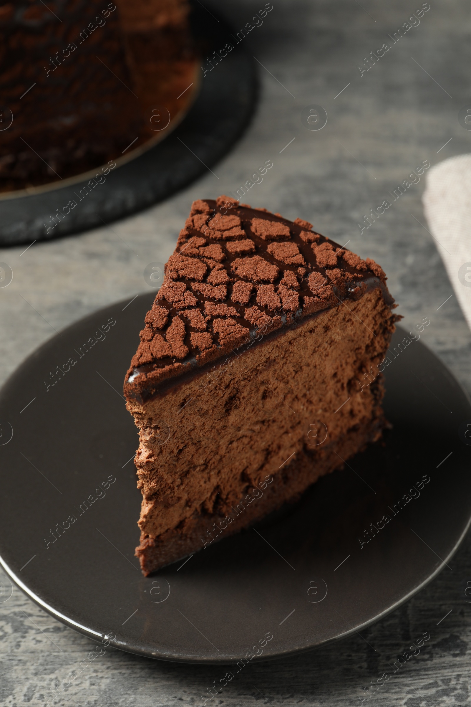 Photo of Piece of delicious chocolate truffle cake on grey textured table, closeup