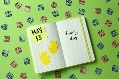 Photo of Happy Family Day. Notebook with text and decorative paper clips on light green background, flat lay