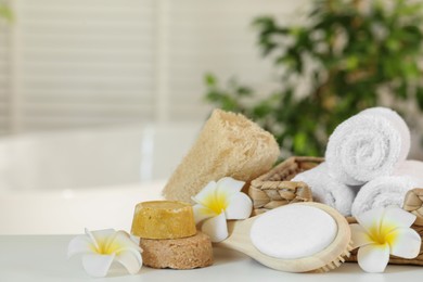 Composition with different spa products and plumeria flowers on white table in bathroom. Space for text