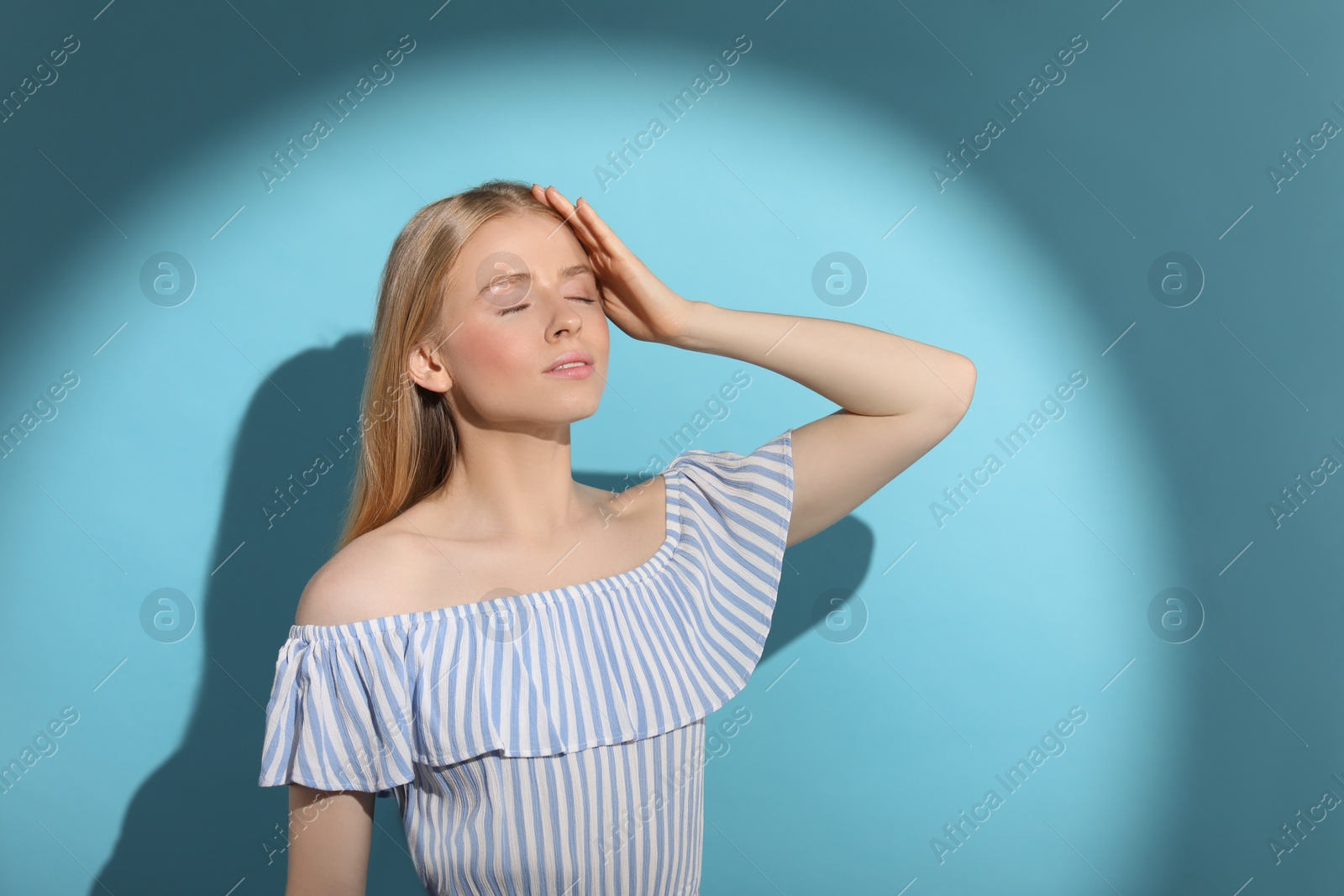 Photo of Beautiful young woman in sunlight on light blue background. Space for text