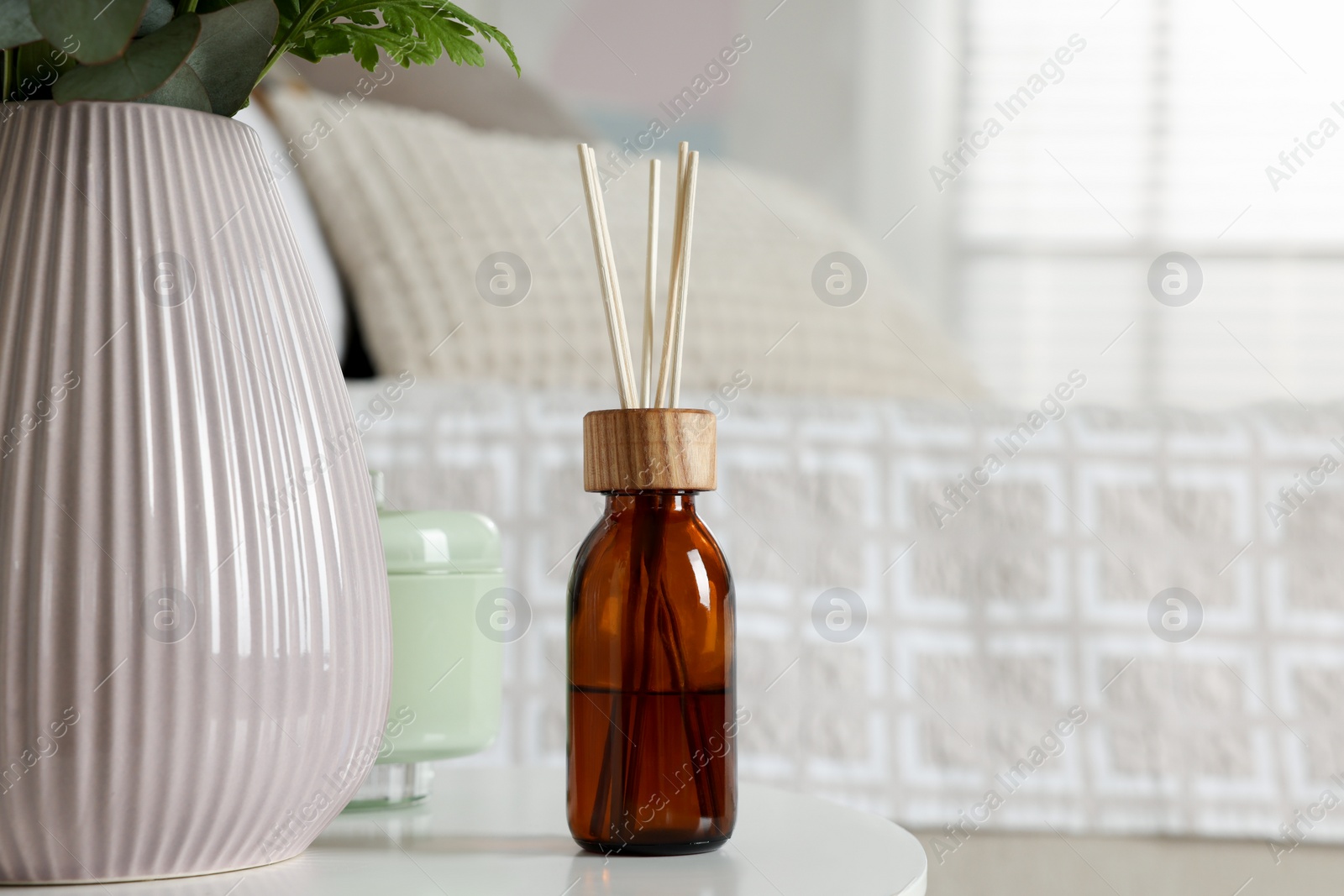 Photo of Aromatic reed air freshener on white table in bedroom. Space for text