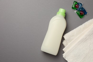 Photo of Bottle of fabric softener, terry towels and laundry detergent pods on gray background, flat lay. Space for text