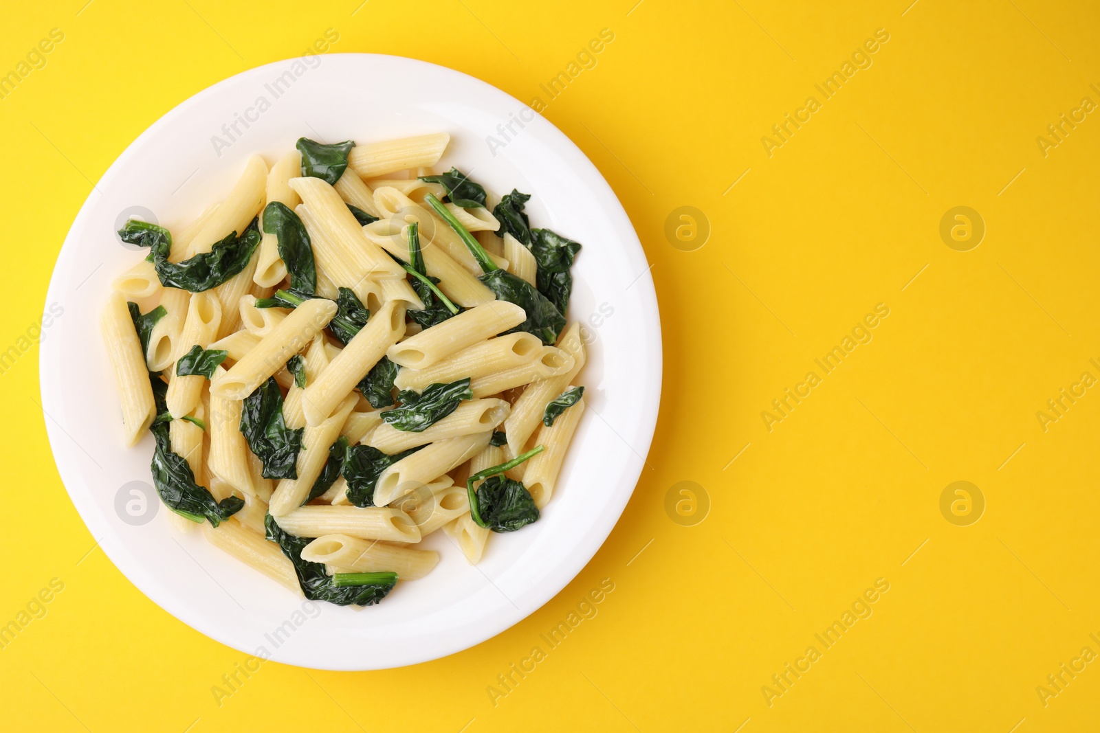 Photo of Tasty pasta with spinach and sauce on yellow table, top view. Space for text