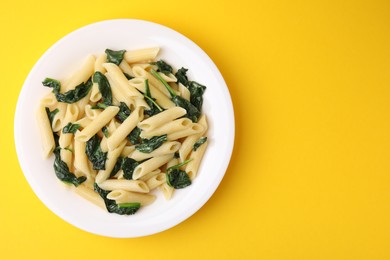 Photo of Tasty pasta with spinach and sauce on yellow table, top view. Space for text