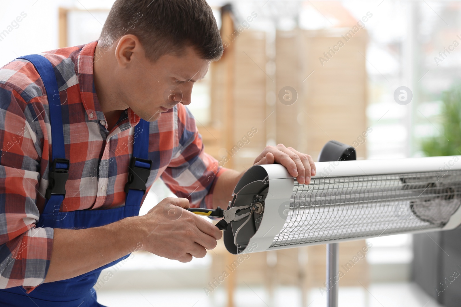 Photo of Professional technician repairing electric infrared heater with pliers indoors