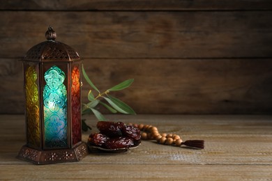 Photo of Arabic lantern, dates and misbaha on wooden table. Space for text