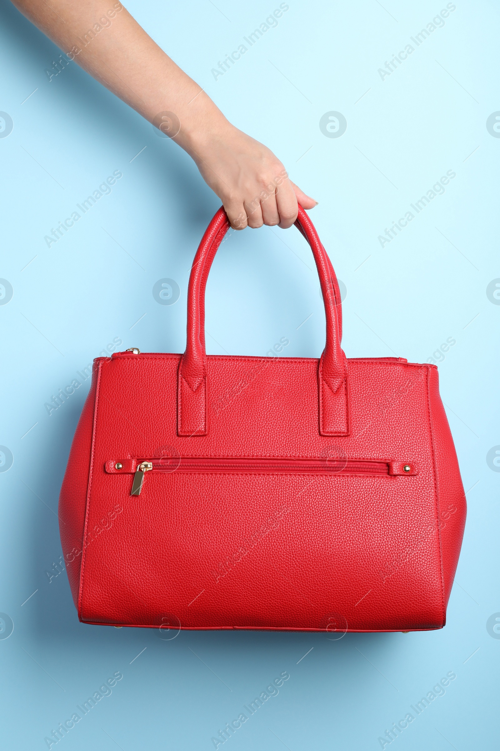 Photo of Woman holding stylish bag on light blue background, closeup