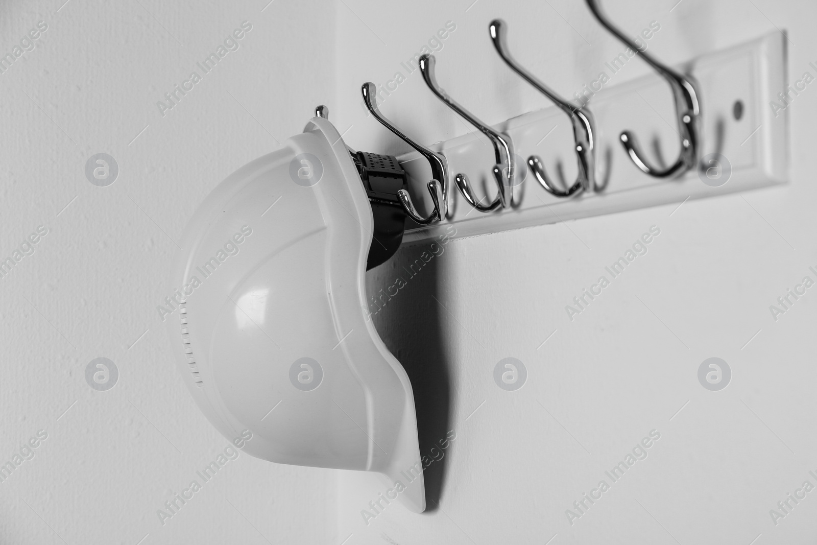 Photo of Hard hat hanging on white wall. Safety equipment