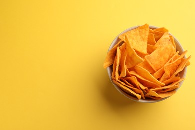 Photo of Tortilla chips (nachos) in bowl on yellow background, top view. Space for text