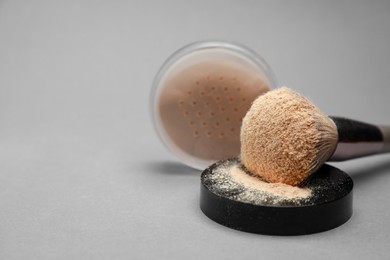 Loose face powder and makeup brush on light grey background, closeup. Space for text