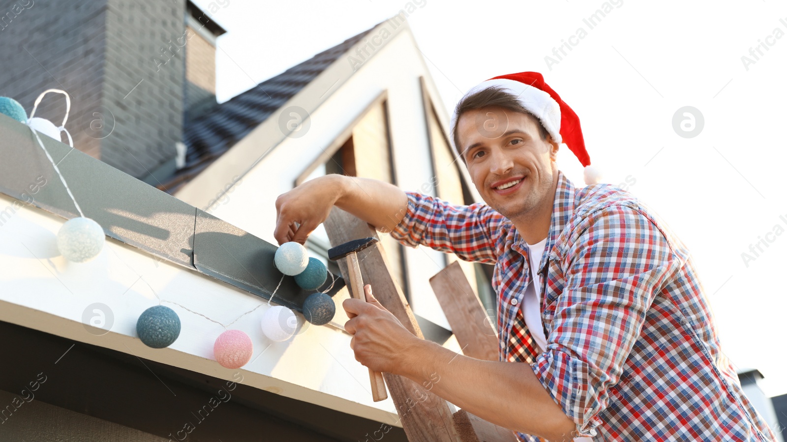 Photo of Man in Santa hat decorating house with Christmas lights outdoors