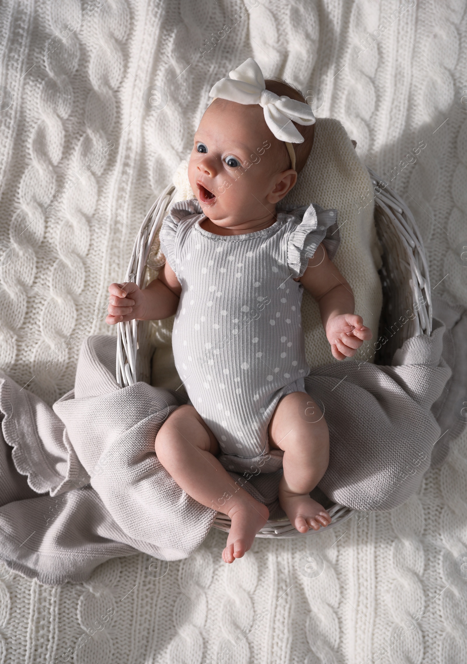 Photo of Adorable newborn baby in basket on bed, top view