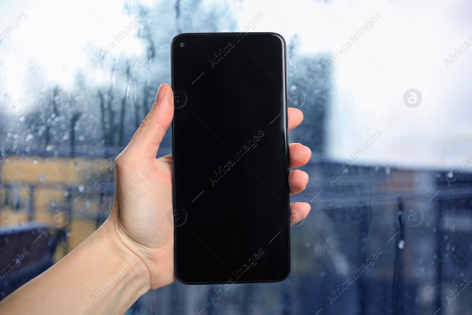 Photo of Woman holding smartphone with blank screen near window, closeup