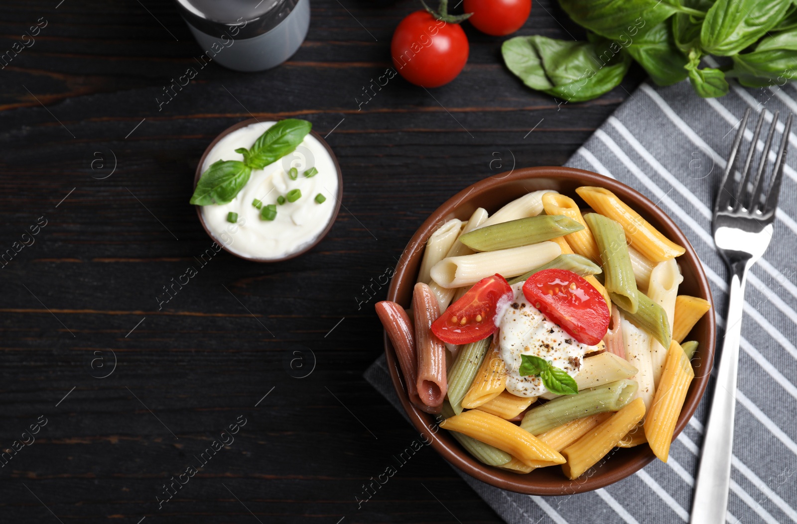 Photo of Delicious vegetable pasta with sour cream dressing on black wooden table, flat lay