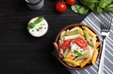 Delicious vegetable pasta with sour cream dressing on black wooden table, flat lay