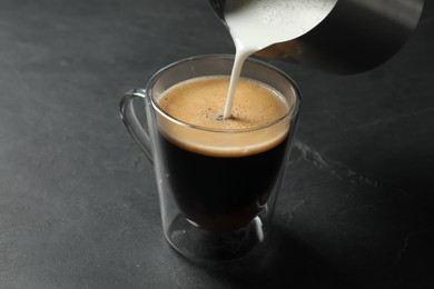 Pouring milk into cup of coffee on black table
