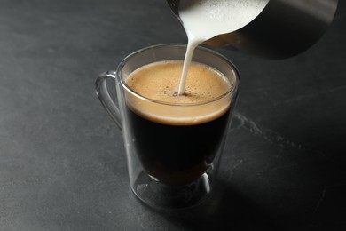 Photo of Pouring milk into cup of coffee on black table