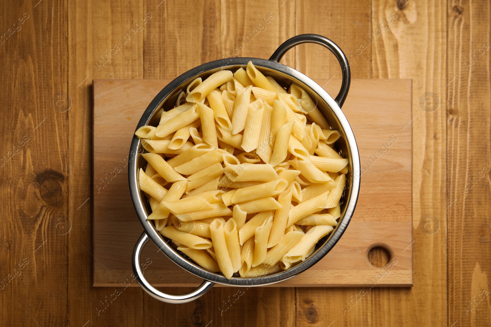 Photo of Cooked pasta in metal colander on wooden table, top view