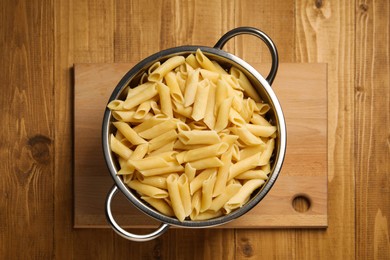 Cooked pasta in metal colander on wooden table, top view