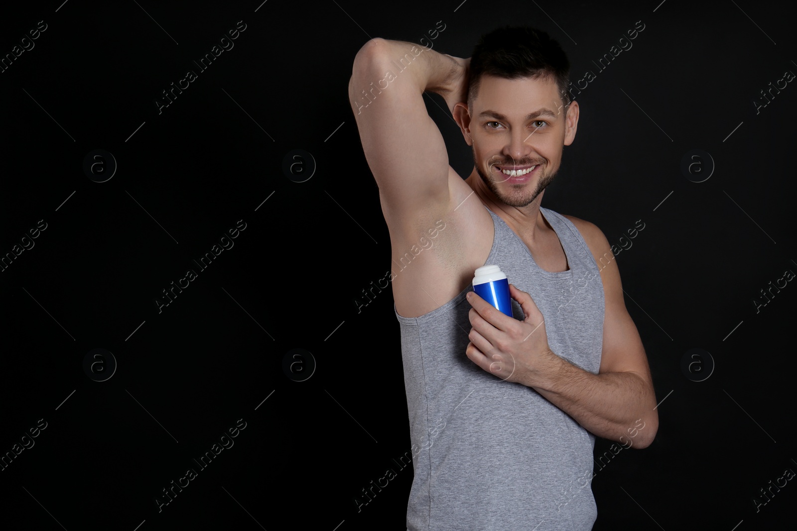 Photo of Handsome man applying deodorant on black background. Space for text