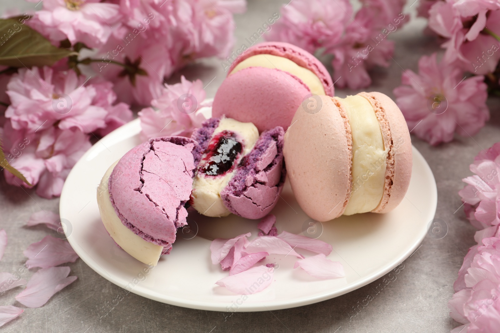 Photo of Delicious colorful macarons and pink flowers on grey table