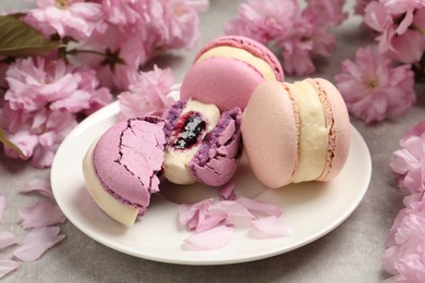 Delicious colorful macarons and pink flowers on grey table