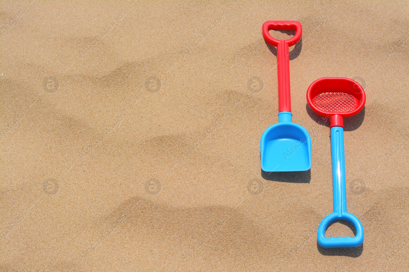 Photo of Plastic shovel and sieve on sand, space for text. Beach toys