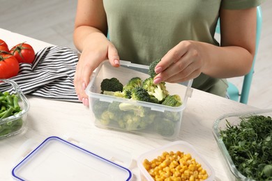 Photo of Woman putting broccoli into plastic container at white wooden table, closeup. Food storage