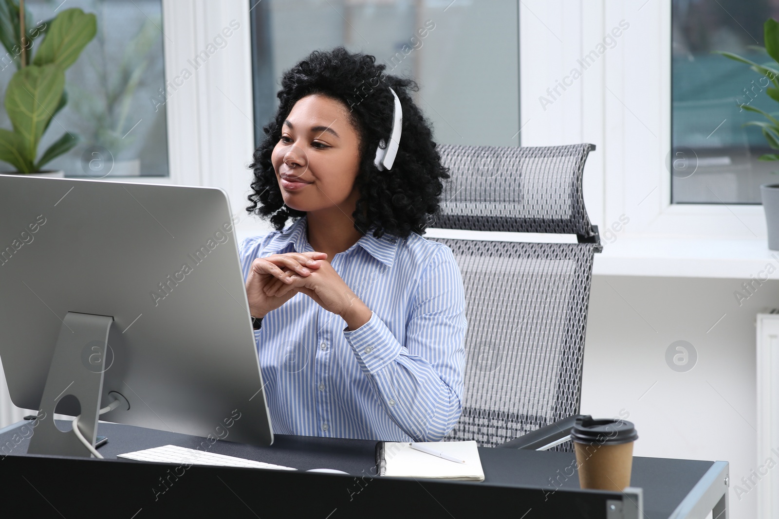 Photo of Young woman with headphones working on computer in office